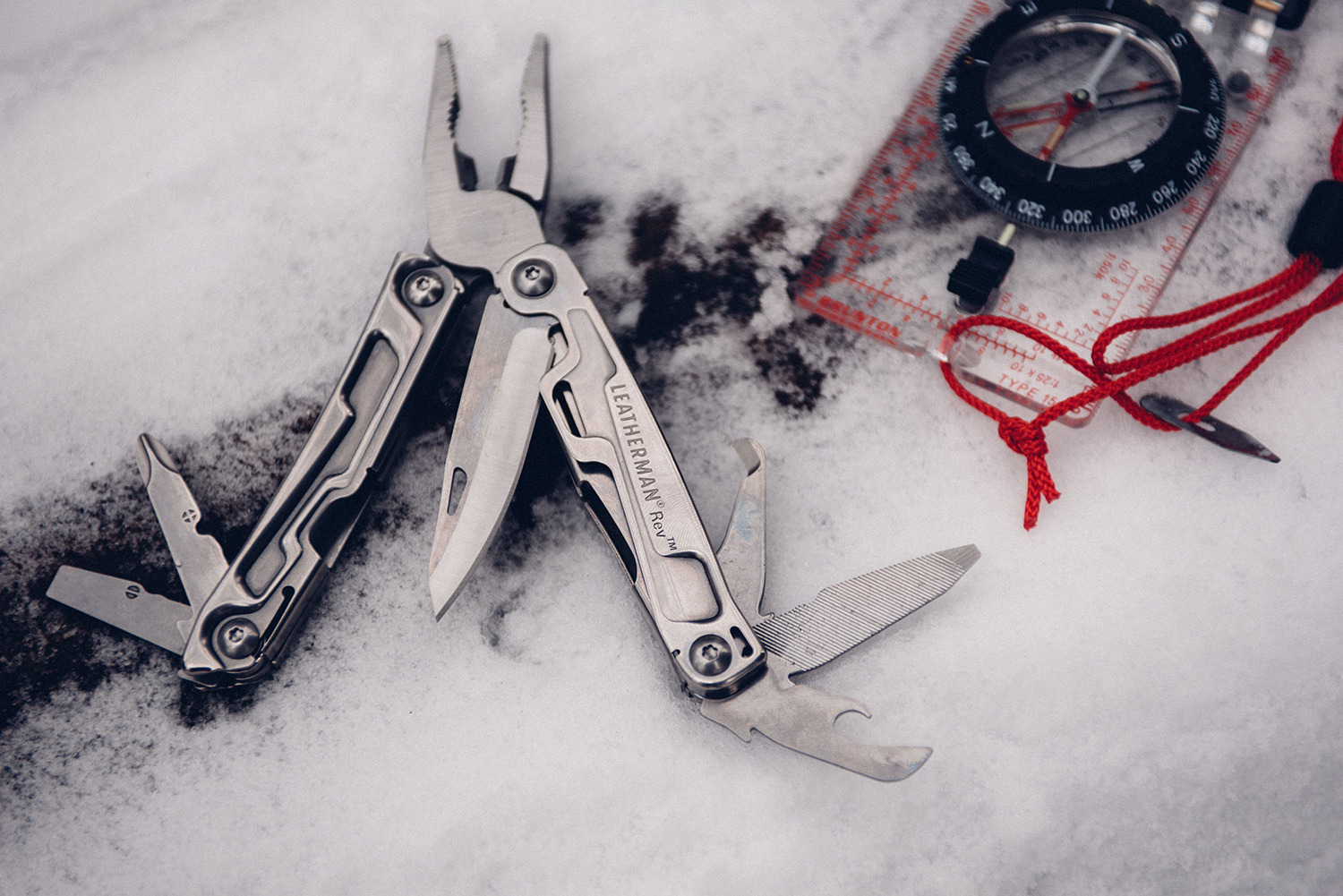 Multi-Tool in snow next to compass.