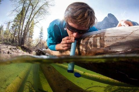 Man drinking through water filtration straw from polluted water.