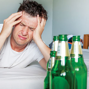 Man with empty bottles of beer holding his head.