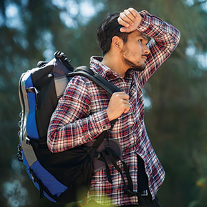 Man with backpack wiping sweat from his head.