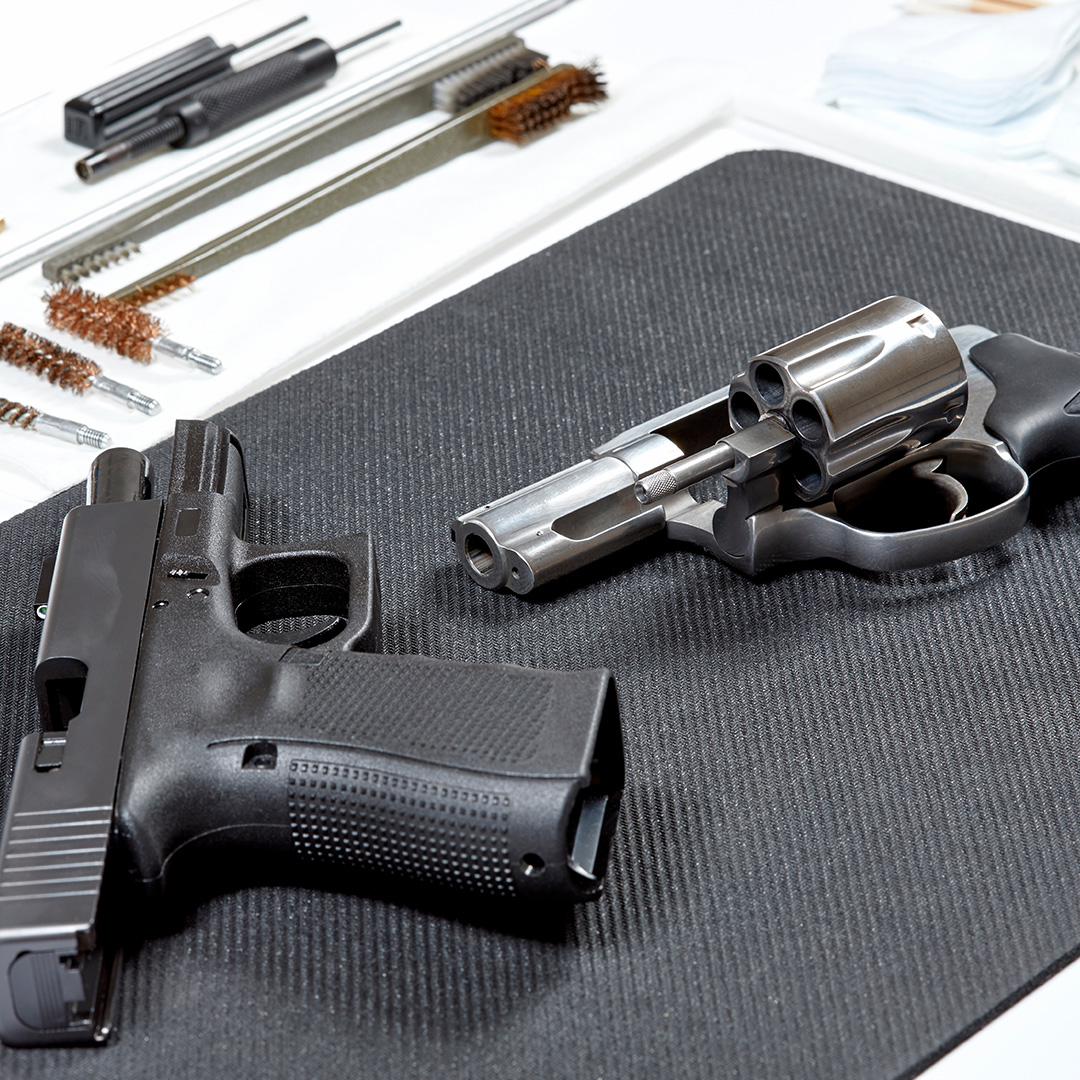 Two handguns on a cleaning mat with bore cleaning rods, brushes, and accessories.