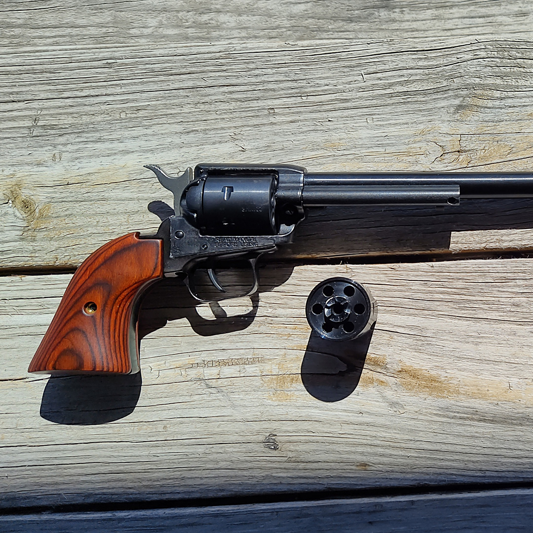 Revolver handgun with extra cylinder on wood background.