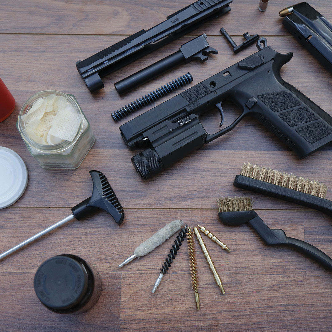 A pistol taken apart with cleaning supplies around it.